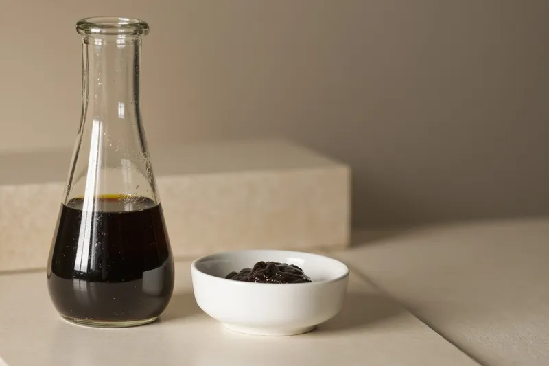 A glass soy sauce bottle next to a small bowl of miso paste on a wooden table