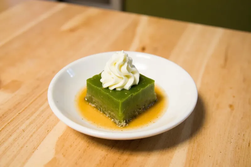 Glass of anmitsu with clear agar jelly cubes, syrup, bean paste and matcha cream
