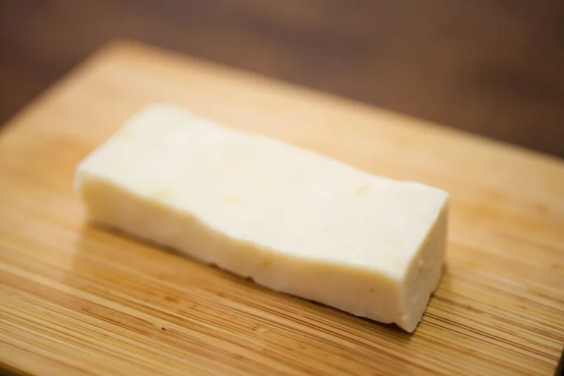 White tofu block placed on a wooden cutting board next to dried nori seaweed sheets